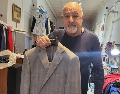 Gregory Chobanian, master tailor serving Lexington, MA, holding a custom-tailored suit jacket in his Waltham shop